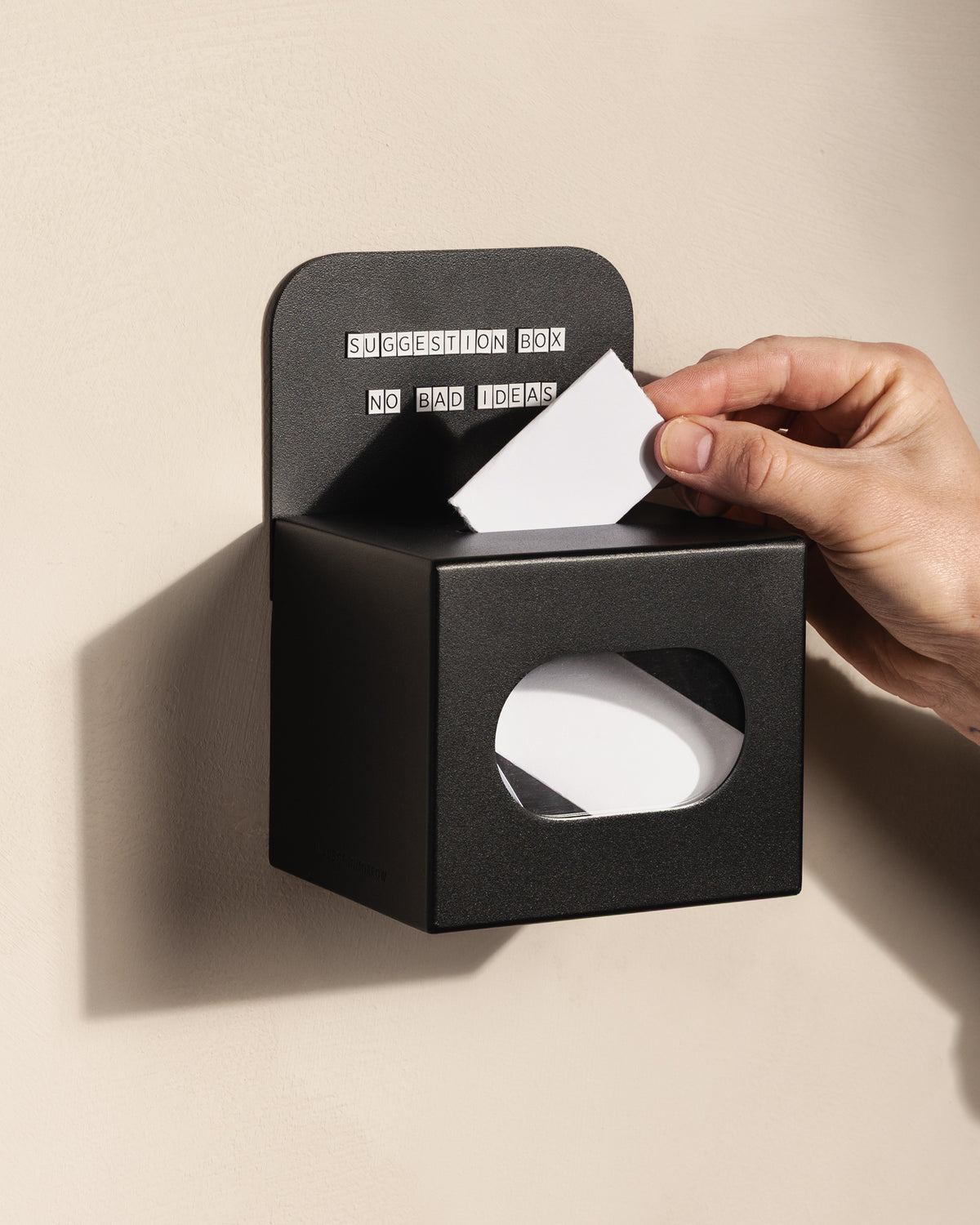 Customer posting a suggestion card into the wall-mounted black FOLD Tip Box