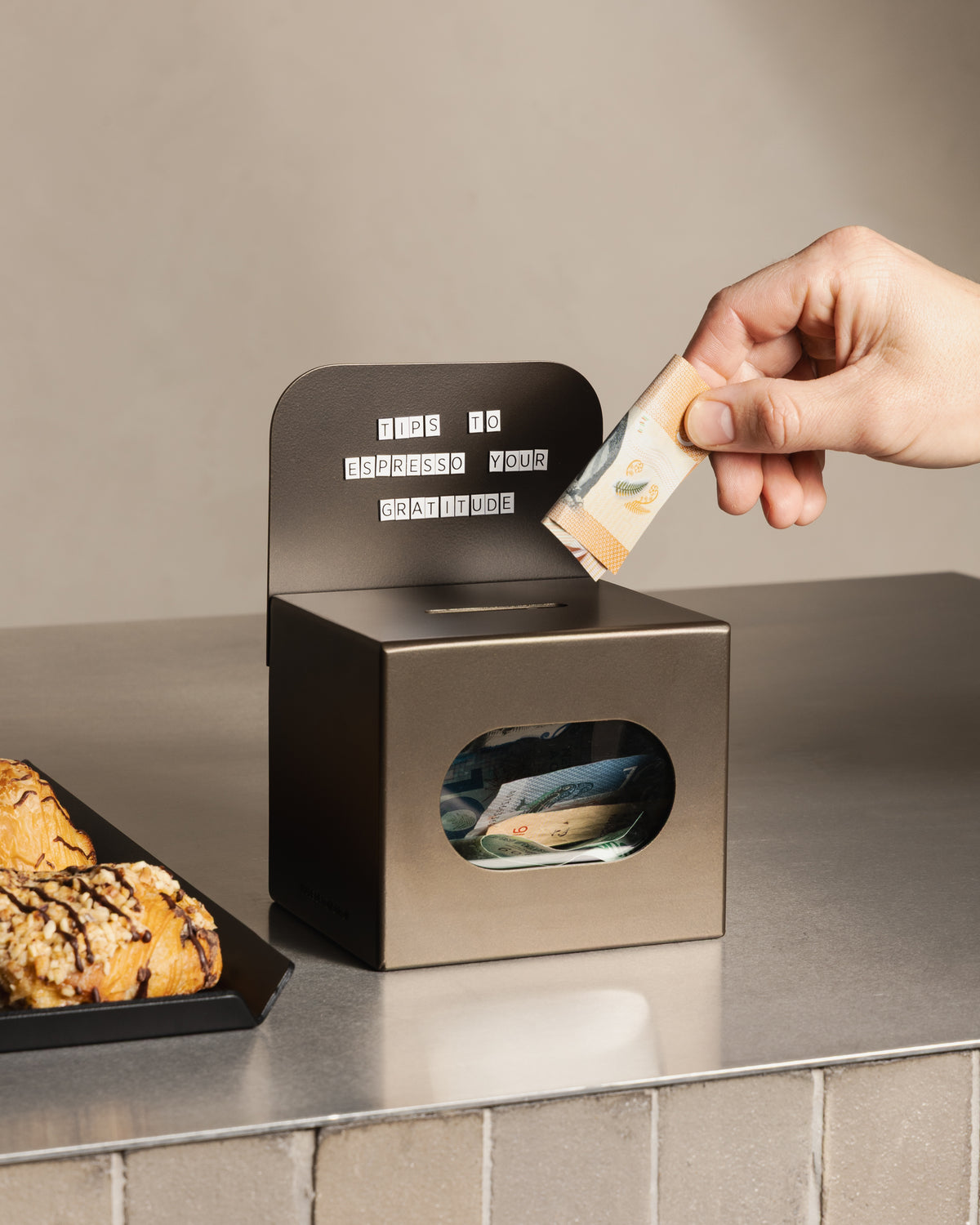 Customer placing a banknote into the bronze FOLD Tip Box on a café counter