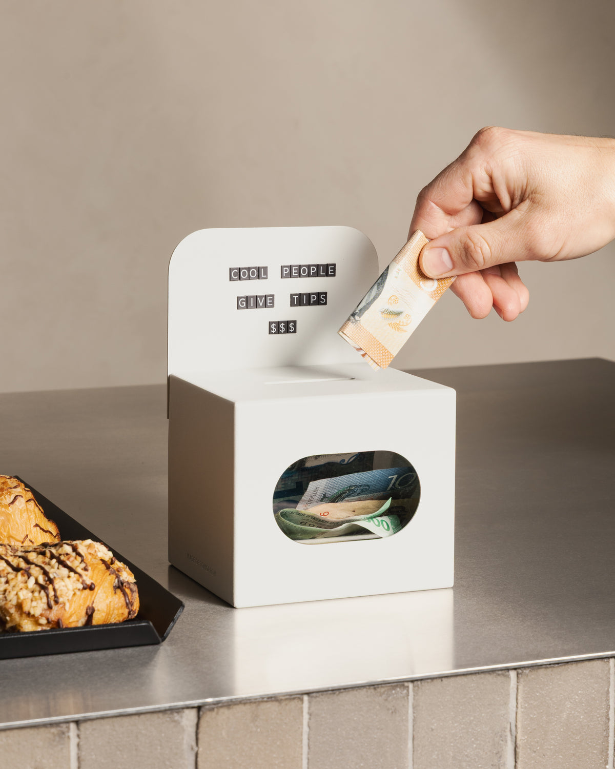 Customer placing a banknote into the white FOLD Tip Box on a café counter
